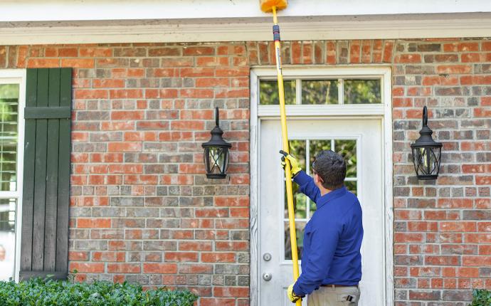 a pest expert removing spider webs outside a home