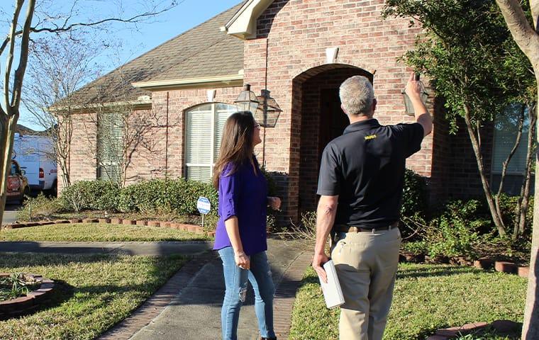 Find Out More About Our Home Pest Control Services a pest control technician and a homeowner inspect the exterior of a home in anahuac texas