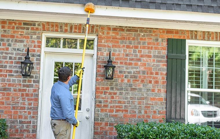 a pest technician removing spider webs outside of a home in modesto california