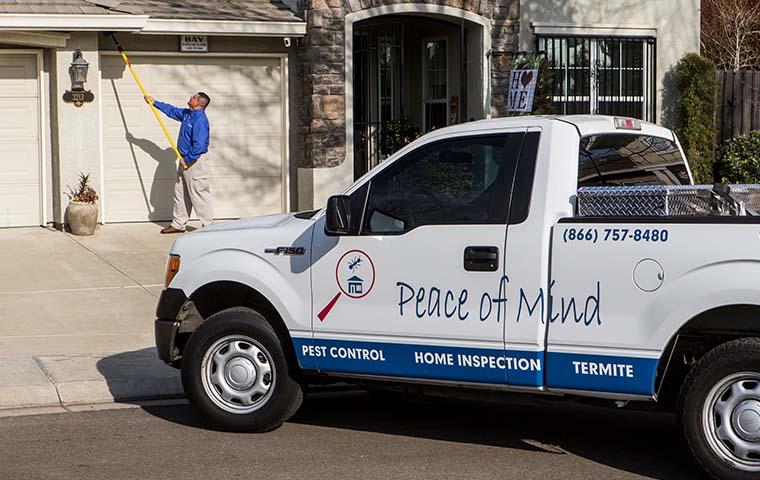 a pest technician removing spider webs outside of a home in modesto california with pest control truck in foreground