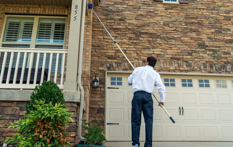 a pest control service technician performing dewebbing services on the exterior of a home in raleigh north carolina