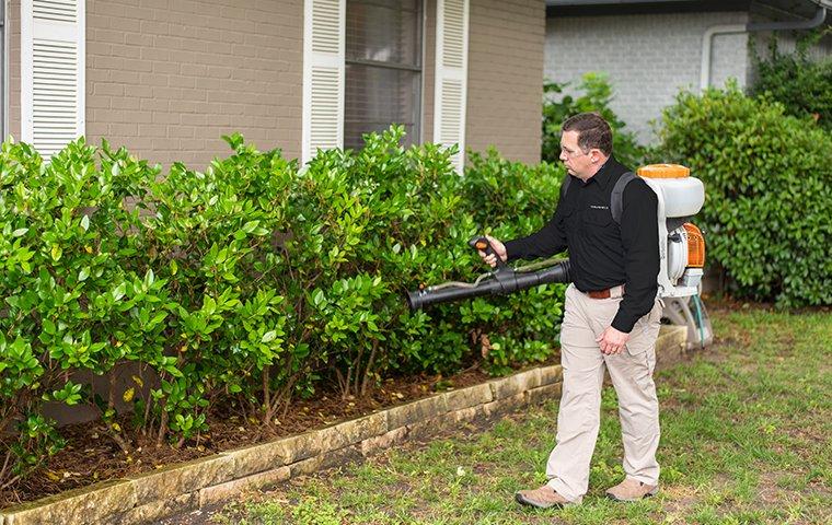 a pest control service technician performing mosquito misting services on the exterior of a home