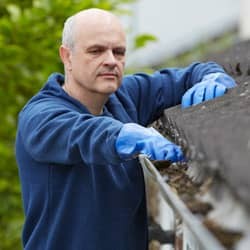 homeowner cleaning his gutter in the spring