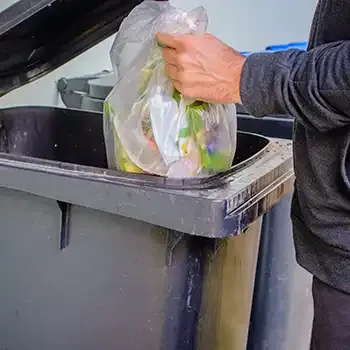 person putting garbage bag into garbage can