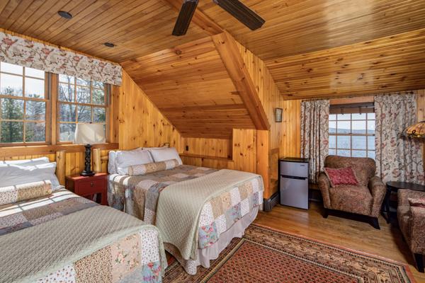 Two beds, two chairs, and a mini-fridge in a wood paneled room