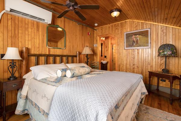 A bed, mirror, lamp, and ceiling fan in a wood paneled room