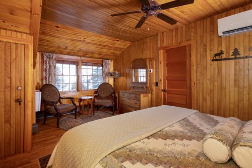 A bed, two chairs, a dresser, and a mirror in a wood paneled room