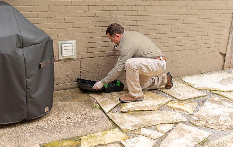 Our Rodent Control Is Perfect For Homes & Businesses a service technician checking a rodent trap outside of a home in lakeway texas