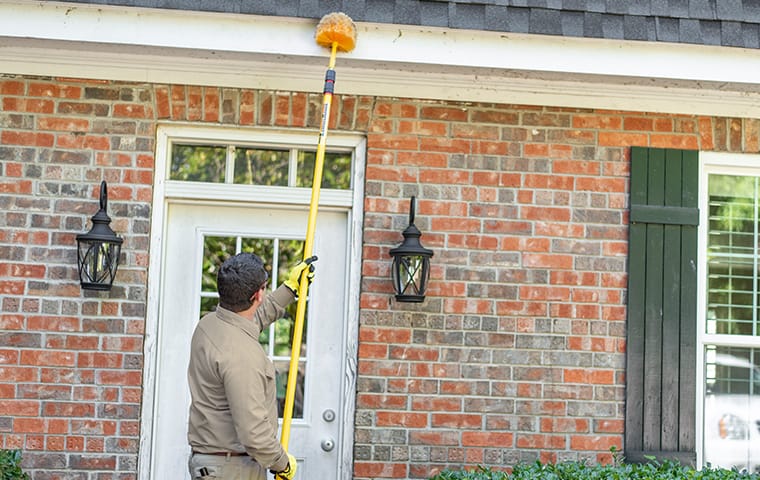 a pest technician removing spider webs from the front of a house in round rock texas