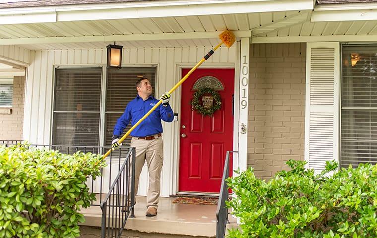 We Protect Homes From Pests Like Spiders & Rodents a service technician clearing spider webs away at a home in lexington south carolina