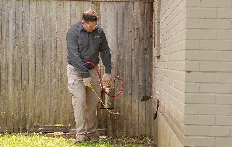 a pest control service technician performing pest treatment services outside of a home