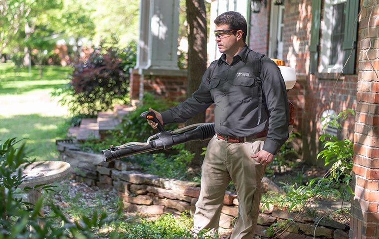 a pest control service technician performing mosquito misting services outside of a home