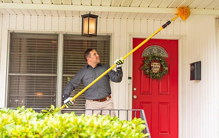 a pest control technician removing spider webs from the doorway of a home in hendersonville north carolina