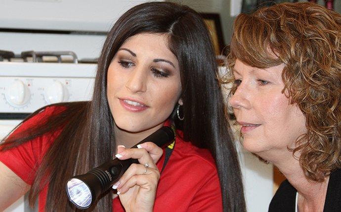 woman pest control technician with flashlight and woman with black shirt