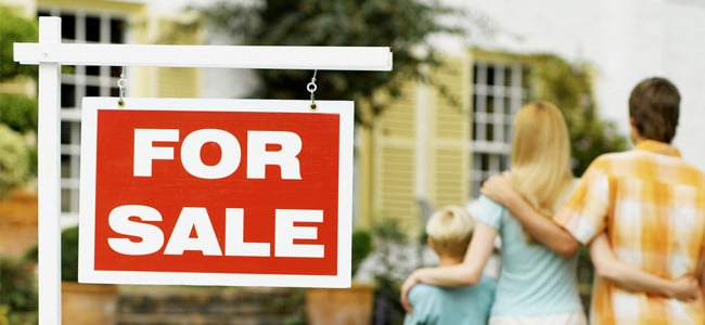 a three person family standing beside a for sale sign in front of a new home