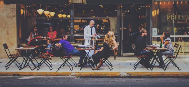 an outdoor seating area at a restaurant with a waiter taking orders from diners