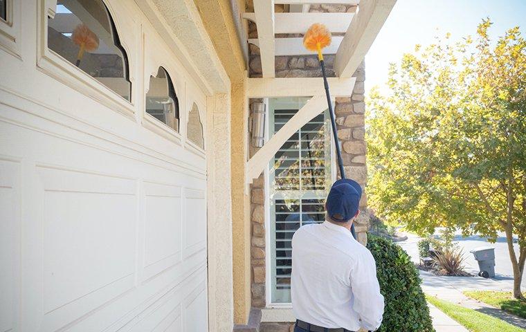 a pest technician removing spider webs outside a home