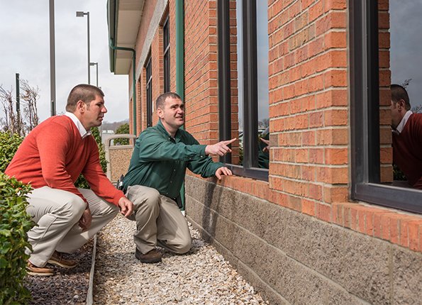 two pest control technicians inspecting the exterior of a brick home