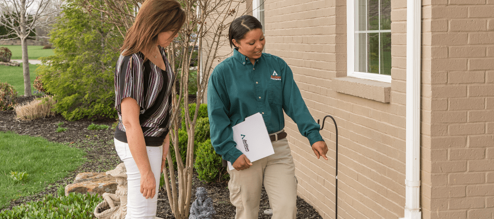 pest control professional with customer looking at the exterior of a home