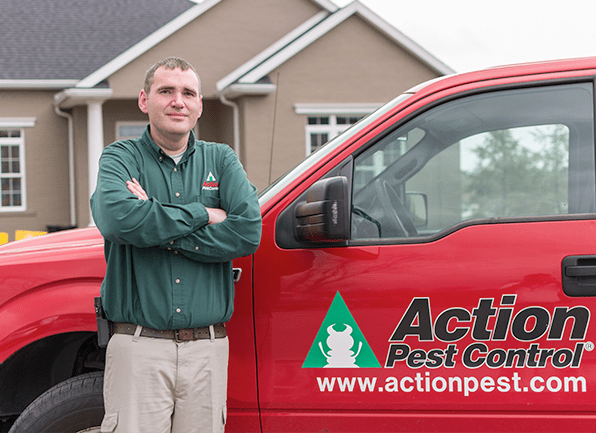pest control professional in front of red truck that has action pest control logo and website