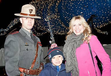 women and son with police officer in front of holiday lights