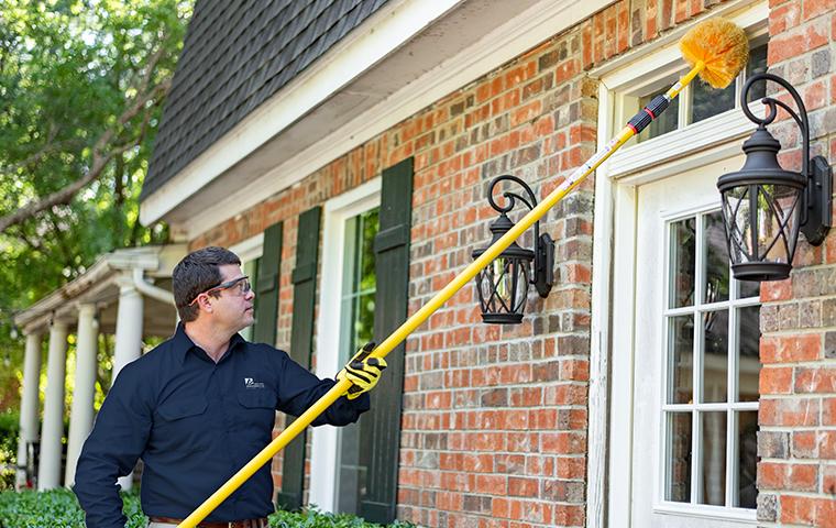 a pest control service technician performing dewebbing services on the exterior of a home