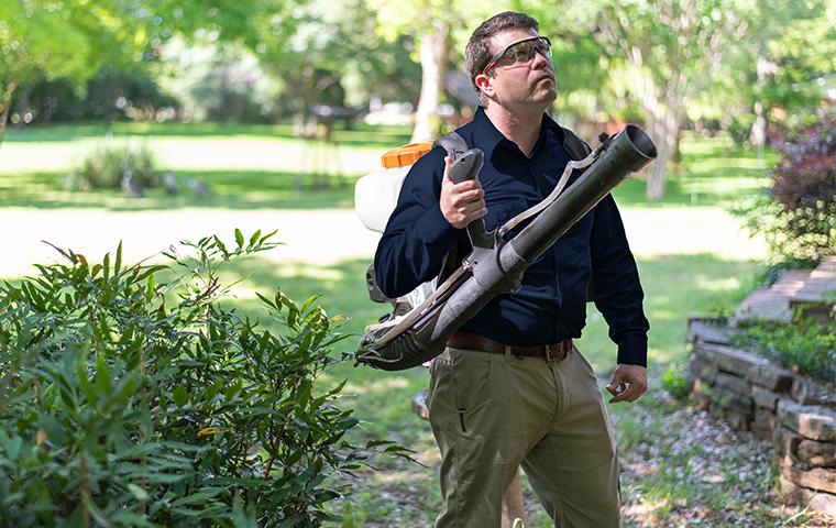 a pest control service technician performing mosquito misting services outside a home