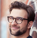 man with glasses smiling next to brick wall