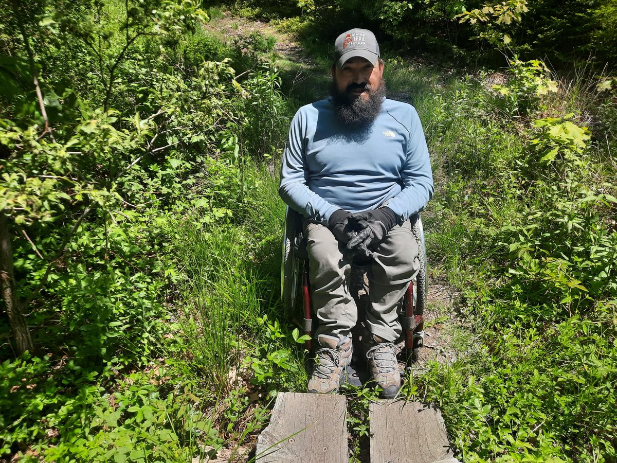 Enock demonstrating the width of the bog bridge compared to his wheelchair.