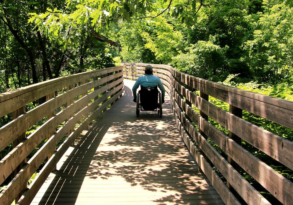 A man in a wheelchair hikes along a boardwalk through the trees