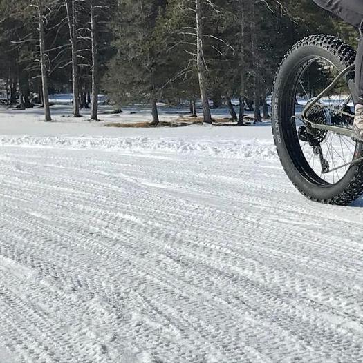 A fat biker bikes over snow following a trail of other bike tracks.