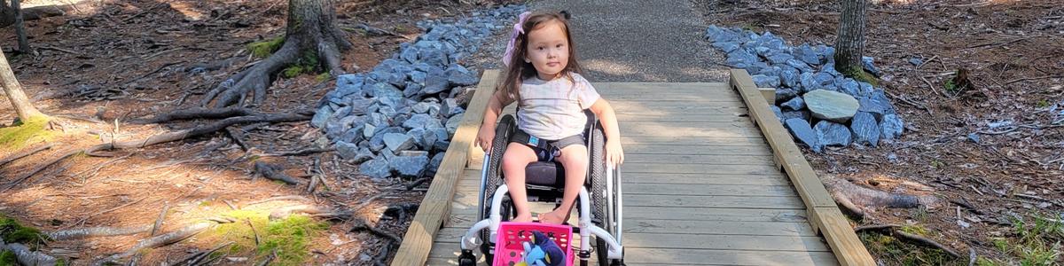 A young girl uses her wheelchair to cross a bridge