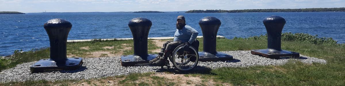 A man using a wheelchair smiles back at the camera with ocean in the background