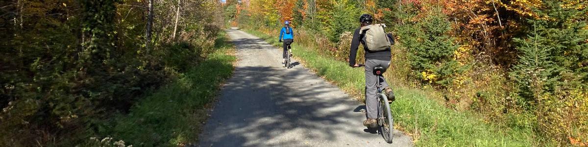 Two cyclists ride on a gravel path in the fall