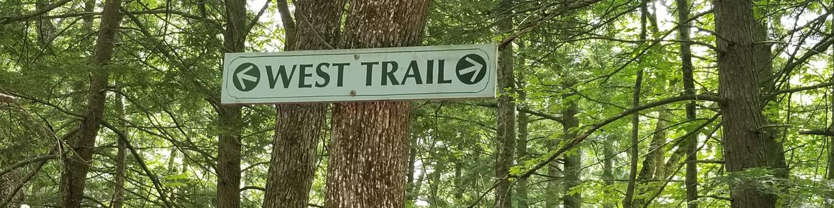 A trail sign for the West Trail with arrows in two directions