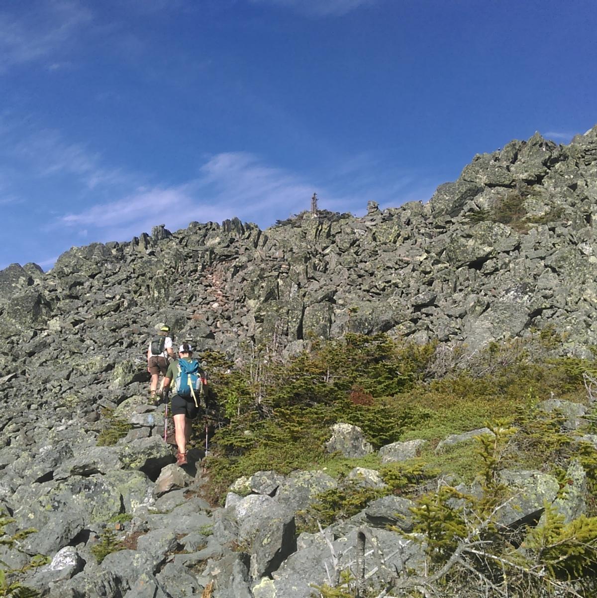 Many jumbled rocks make up the talus slope that two women are hiking over