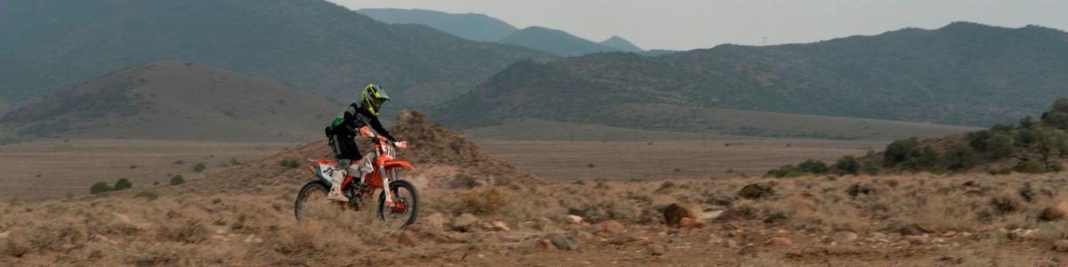 A person dirtbikes through scrubby desert
