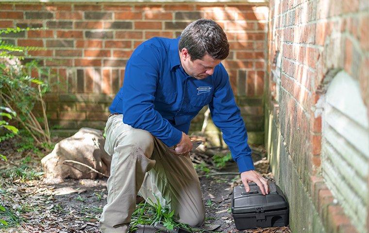 a pest technician checking a rodent trap outside of a home in fairfield connecticut