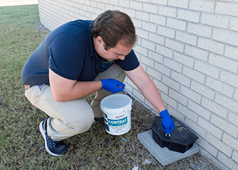 Monthly Rodent Follow-Up Services tech cleaning and baiting rodent station outside tulsa home