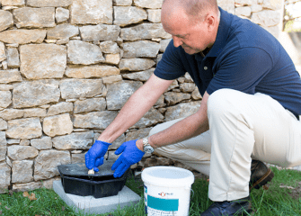 Monthly Rodent Follow-Up Services tech cleaning and baiting rodent station outside tulsa home