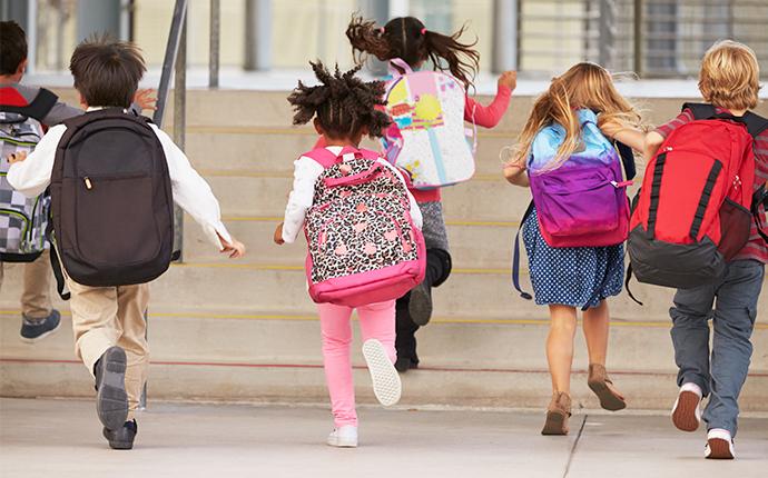 a class of children running into a school building in aware of the threat of spreading bed bugs in their back packs