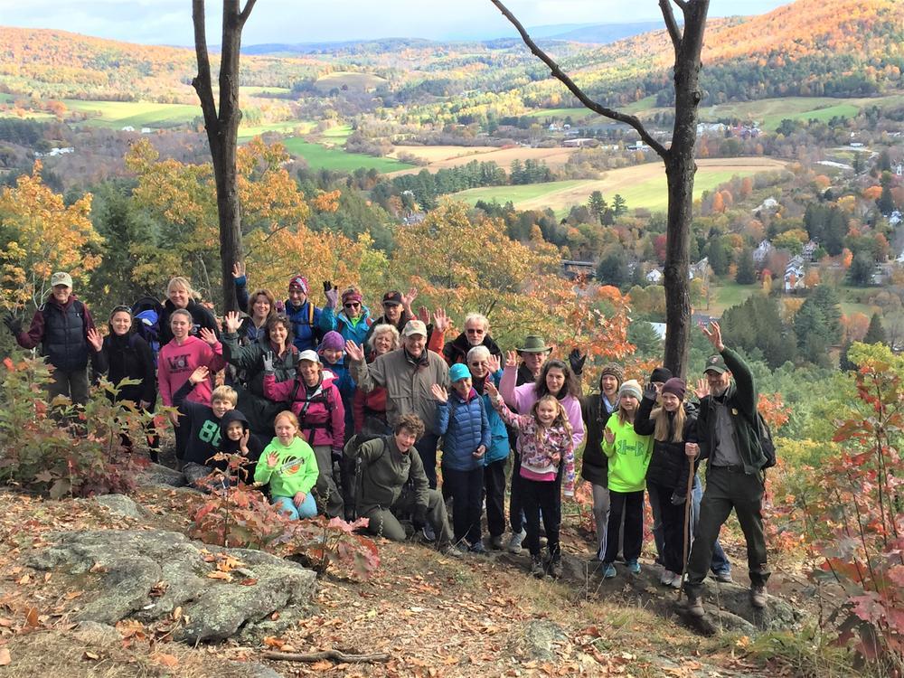 A large group of volunteers stands together and smiles for a photo on Faulkner Trail with a valley landscape in the background.