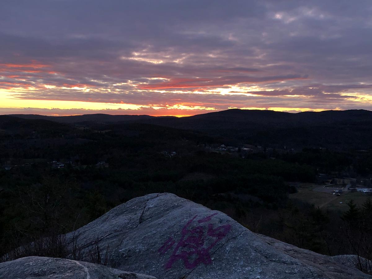 The rocky top of French's Ledges is visible in the foreground, and on the horizon is a purple, orange, and yellow sunrise.