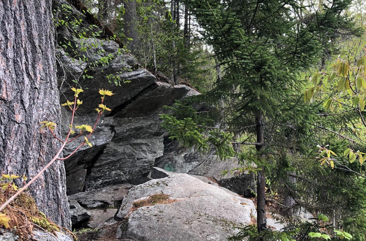 Boulders around ten feet high slope over the trail by the lake.