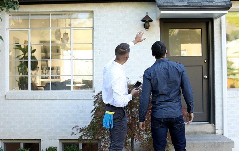 a pest control service technician inspecting the exterior of a home