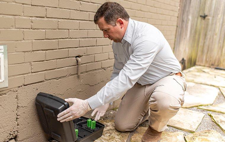 a pest control service technician installing a rodent bait station outside of a home