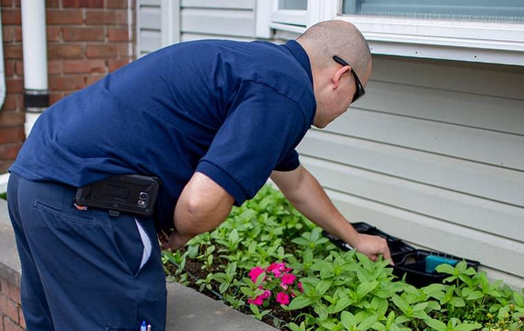 Call Parkway Pest Services To Prevent Rodents From Coming Into Your Home technician inspecting rodent station along side a long island home