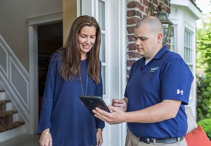 parkway pest services technician reviewing a tablet with a female homeowner on a front porch