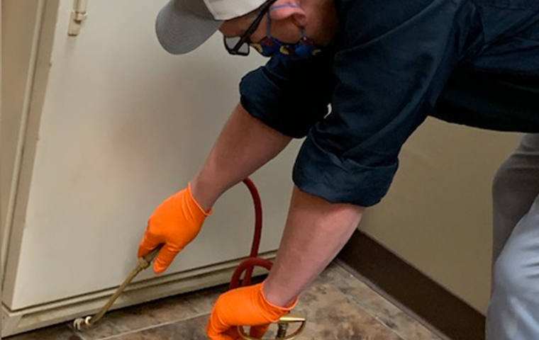 masked dart pest technician applying pest control treatment in a kitchen